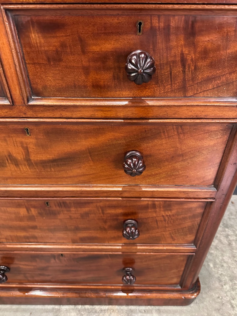 A Victorian flame mahogany chest of drawers featuring two short over three long drawers with turned knobs and a plinth base. View VI