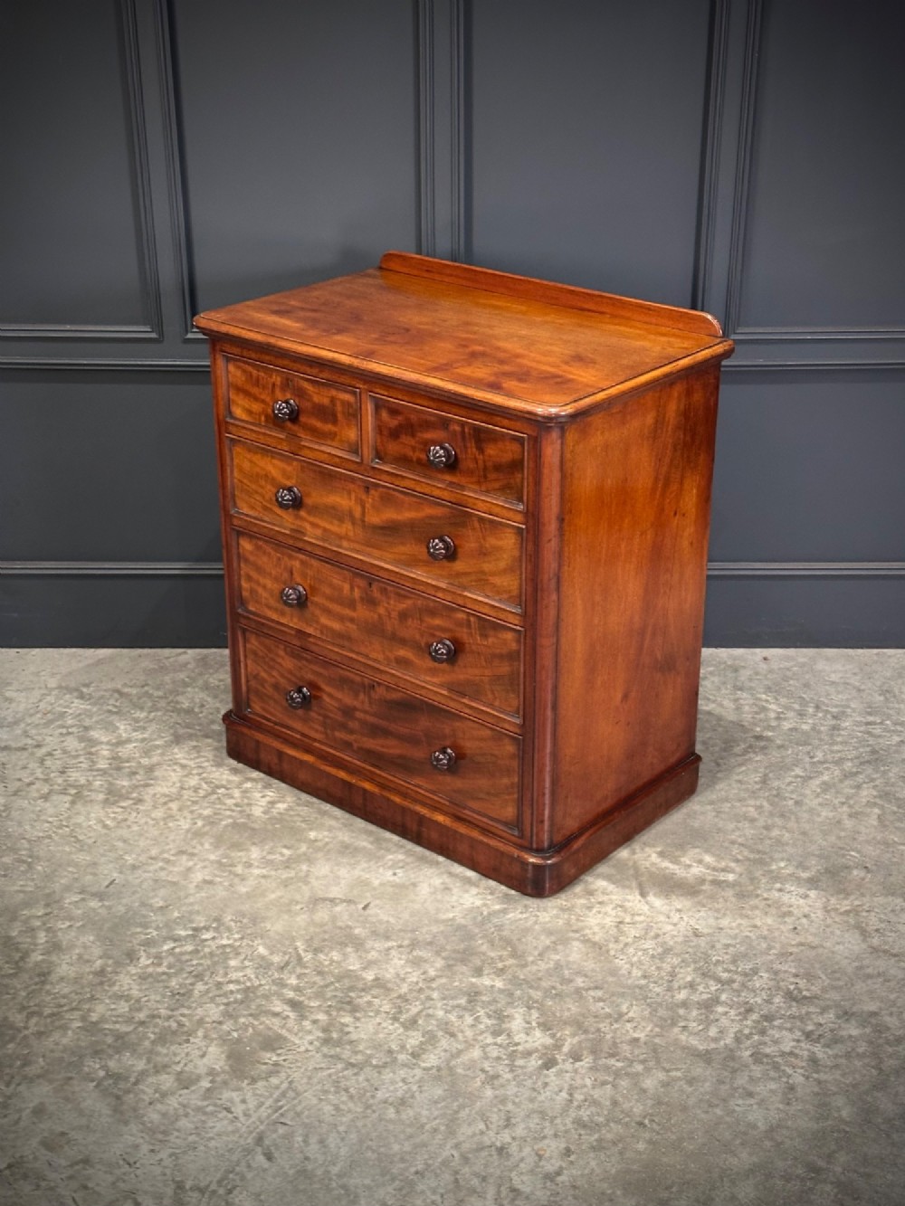 A Victorian flame mahogany chest of drawers featuring two short over three long drawers with turned knobs and a plinth base. View VII