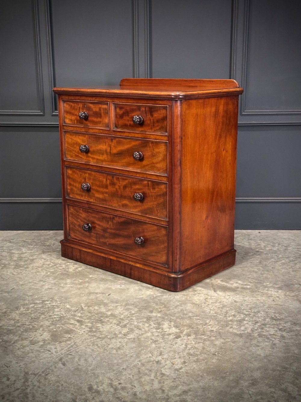 A Victorian flame mahogany chest of drawers featuring two short over three long drawers with turned knobs and a plinth base. View VIII