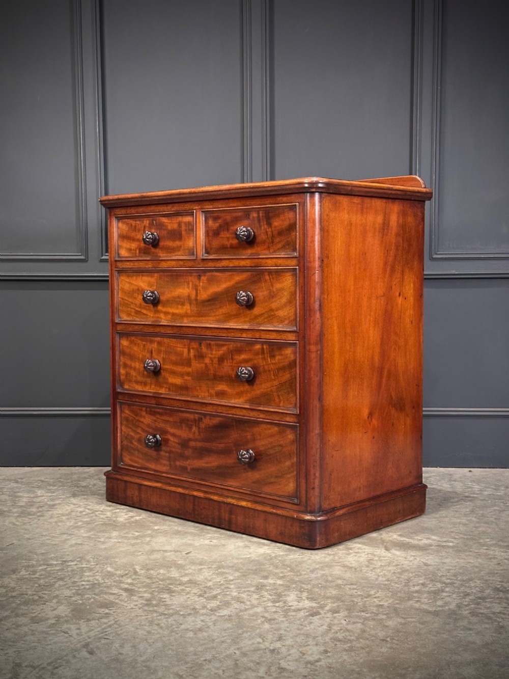 A Victorian flame mahogany chest of drawers featuring two short over three long drawers with turned knobs and a plinth base. View IX