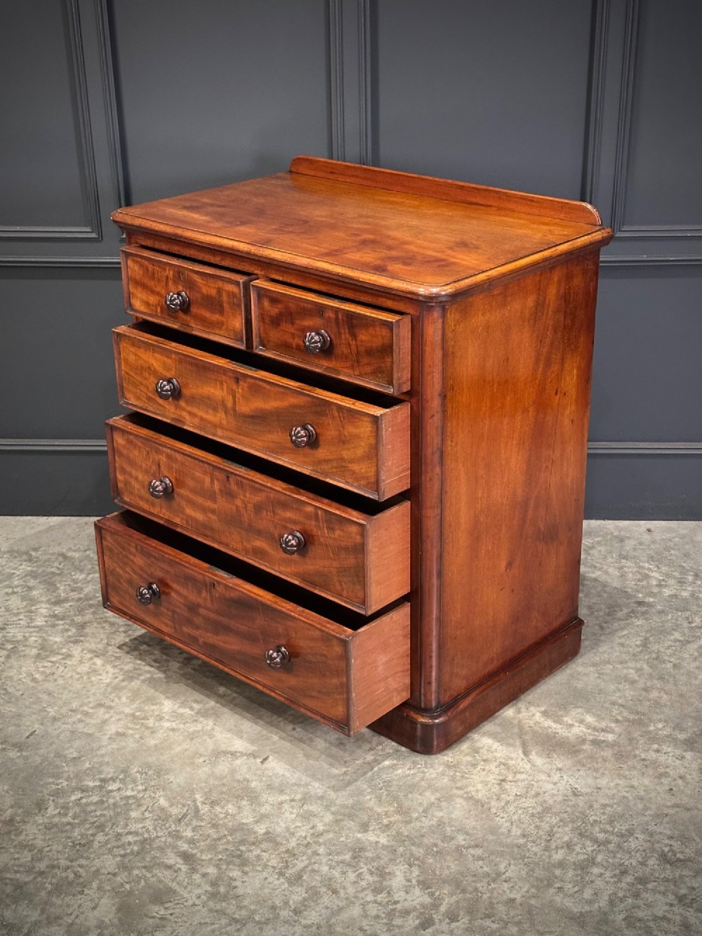 A Victorian flame mahogany chest of drawers featuring two short over three long drawers with turned knobs and a plinth base. View XII