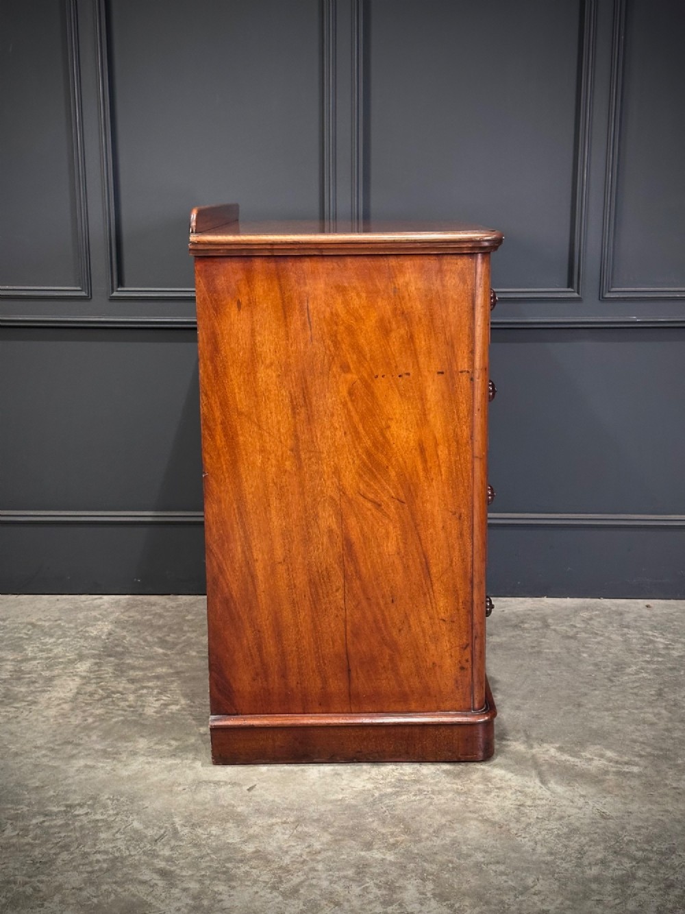 A Victorian flame mahogany chest of drawers featuring two short over three long drawers with turned knobs and a plinth base. View XV