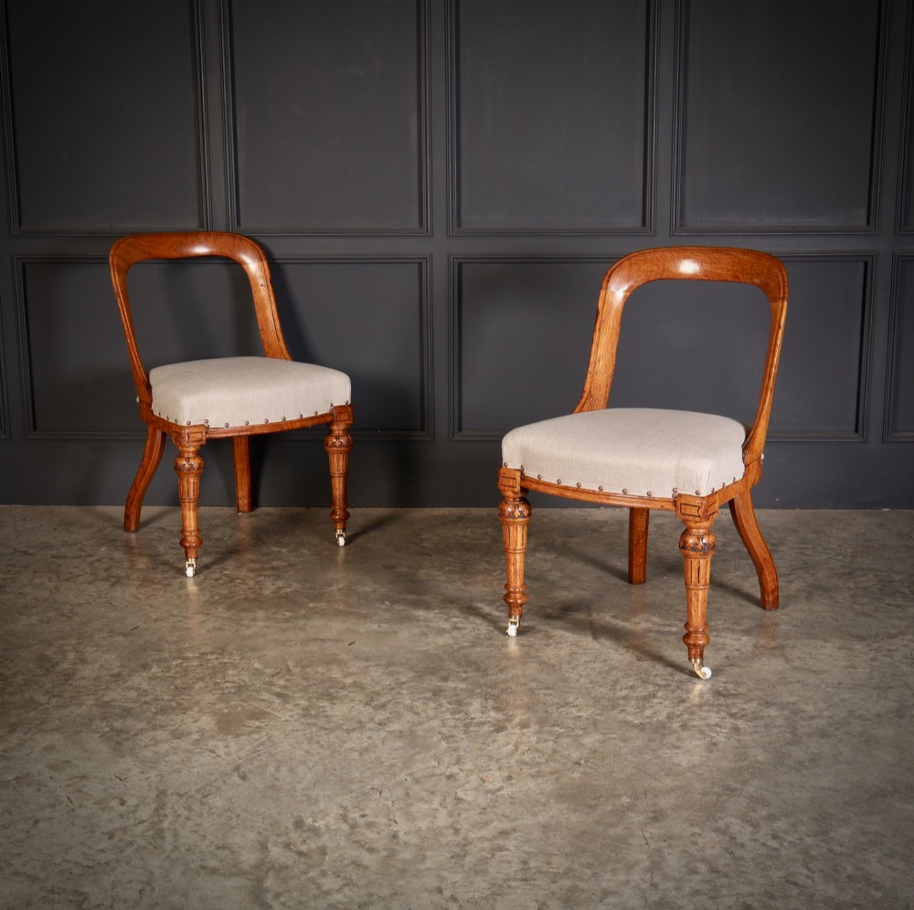 A set of ten Victorian oak dining chairs with rounded hoop backs, neutral fabric seats with stud trim, and carved front legs on ceramic castors. View III