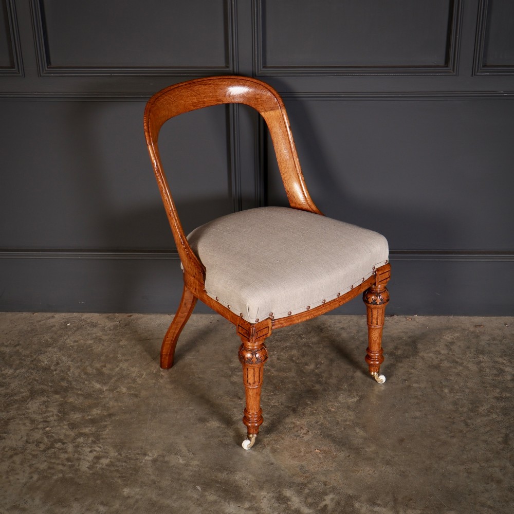 A set of ten Victorian oak dining chairs with rounded hoop backs, neutral fabric seats with stud trim, and carved front legs on ceramic castors. View IV