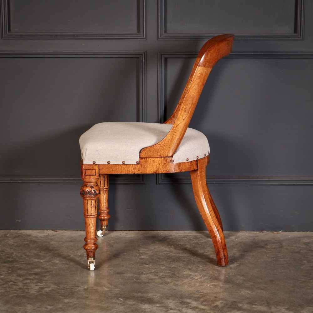 A set of ten Victorian oak dining chairs with rounded hoop backs, neutral fabric seats with stud trim, and carved front legs on ceramic castors. View IX