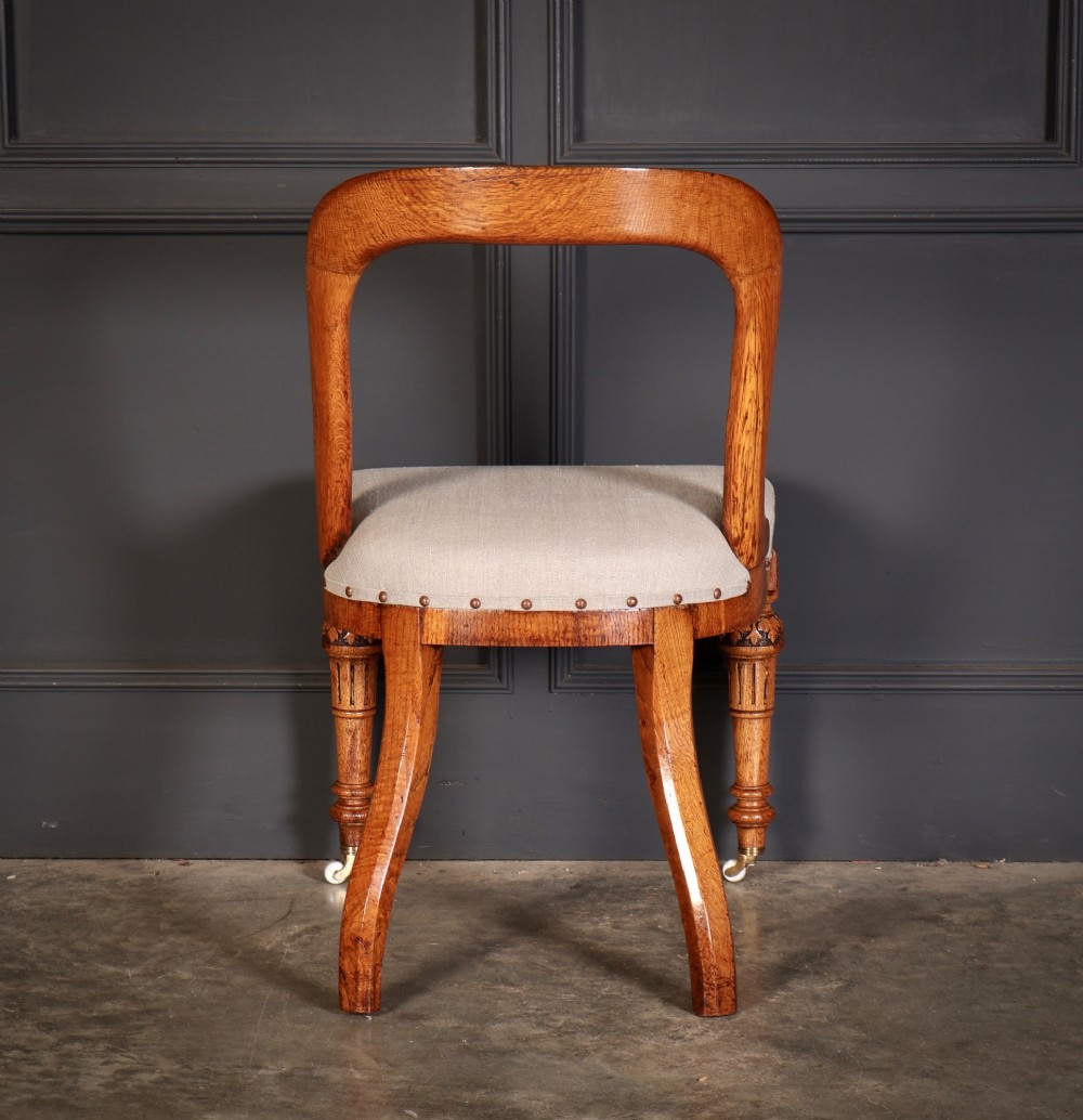 A set of ten Victorian oak dining chairs with rounded hoop backs, neutral fabric seats with stud trim, and carved front legs on ceramic castors. View X