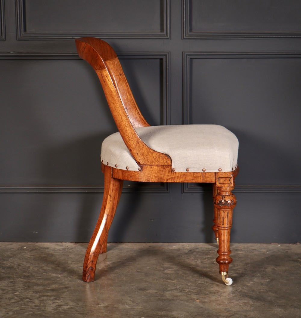 A set of ten Victorian oak dining chairs with rounded hoop backs, neutral fabric seats with stud trim, and carved front legs on ceramic castors. View XI