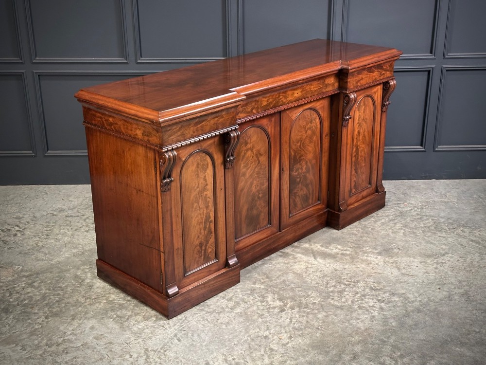 A Victorian flame mahogany four-door sideboard featuring arched panel doors, hand-carved corbel brackets, and a flat plinth base.