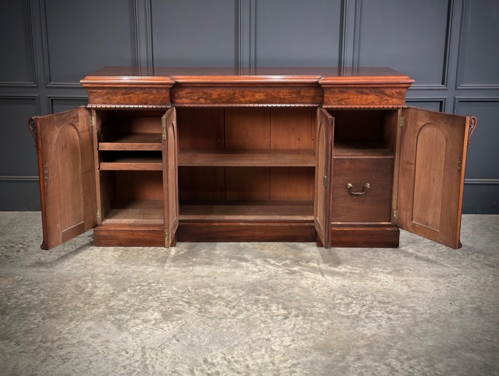 A Victorian flame mahogany four-door sideboard featuring arched panel doors, hand-carved corbel brackets, and a flat plinth base. View V