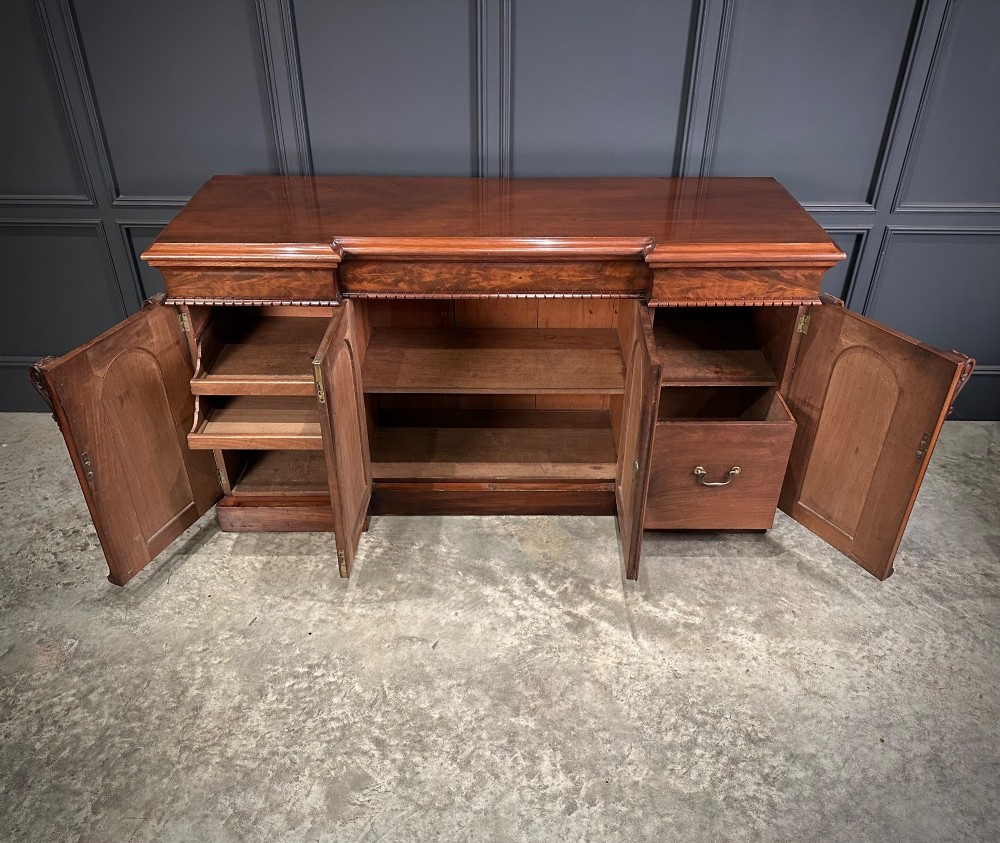A Victorian flame mahogany four-door sideboard featuring arched panel doors, hand-carved corbel brackets, and a flat plinth base. View VIII