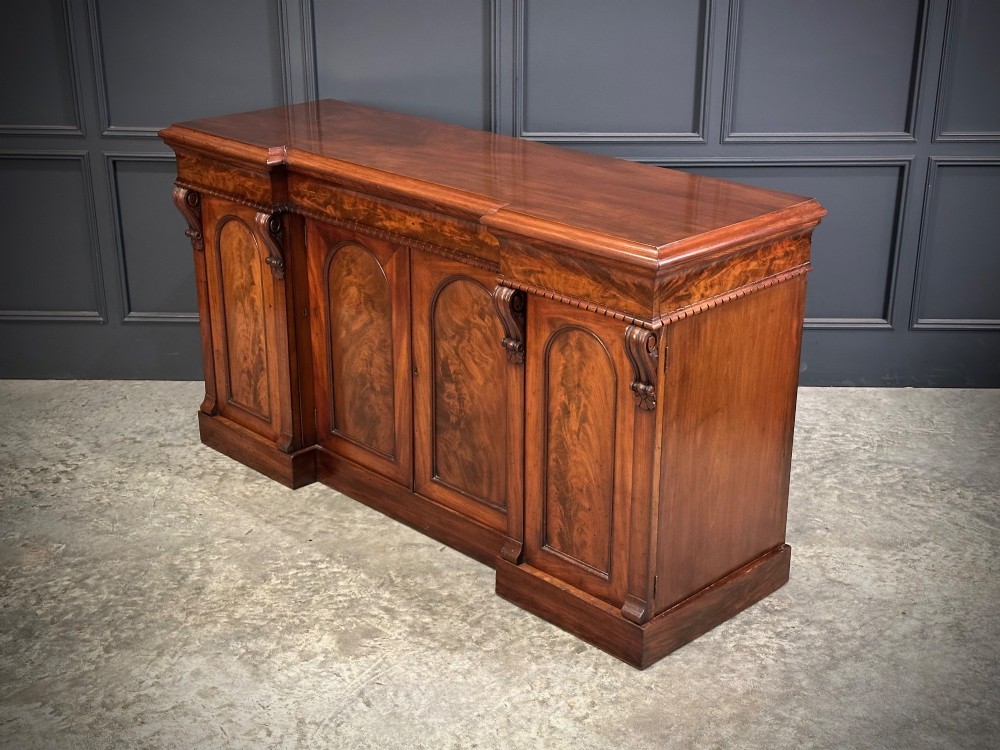 A Victorian flame mahogany four-door sideboard featuring arched panel doors, hand-carved corbel brackets, and a flat plinth base. View IX