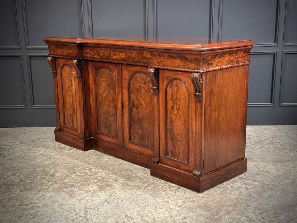 A Victorian flame mahogany four-door sideboard featuring arched panel doors, hand-carved corbel brackets, and a flat plinth base. View X