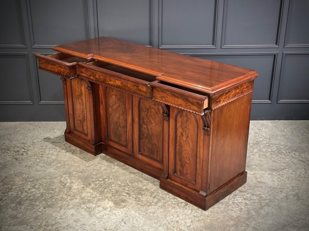 A Victorian flame mahogany four-door sideboard featuring arched panel doors, hand-carved corbel brackets, and a flat plinth base. View XI