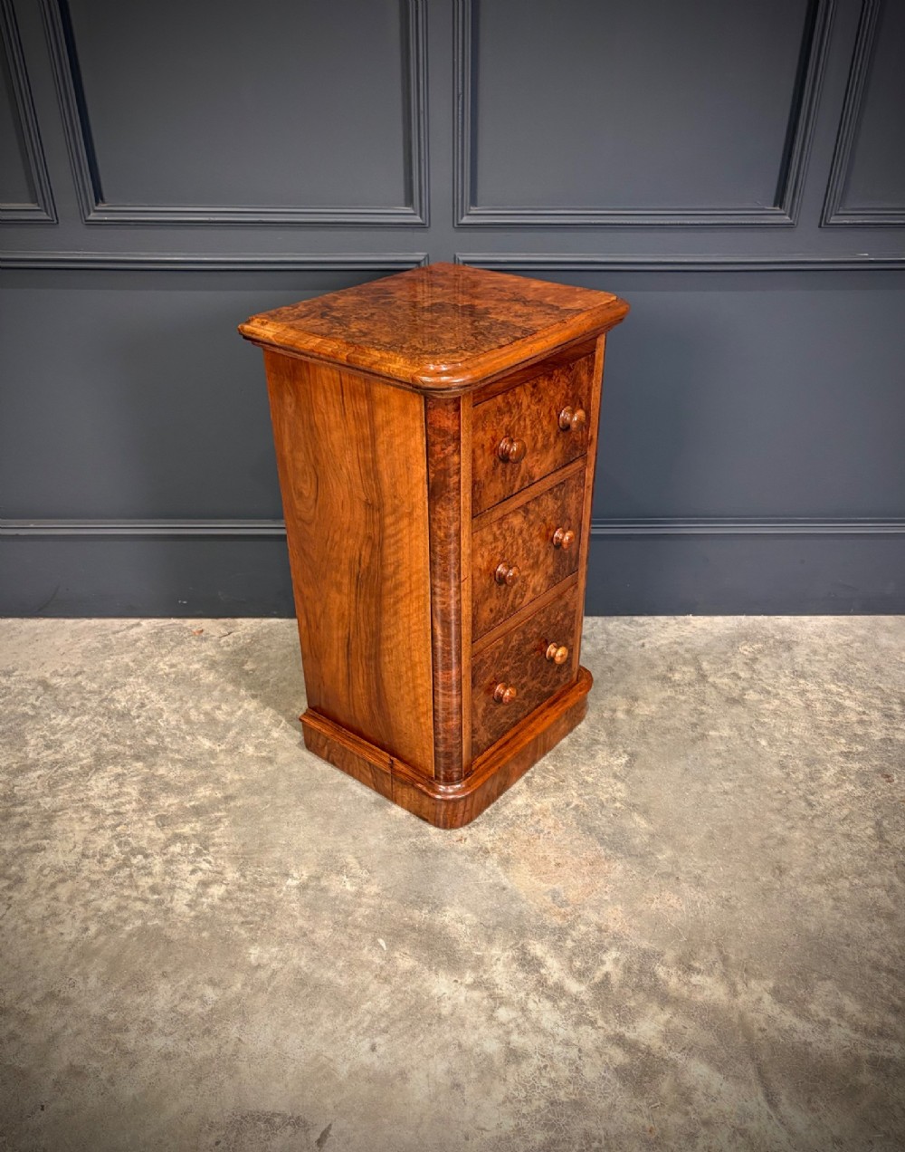 A matching pair of Victorian burr walnut bedside chests featuring three drawers each with turned wooden knobs and rounded plinth bases. View V