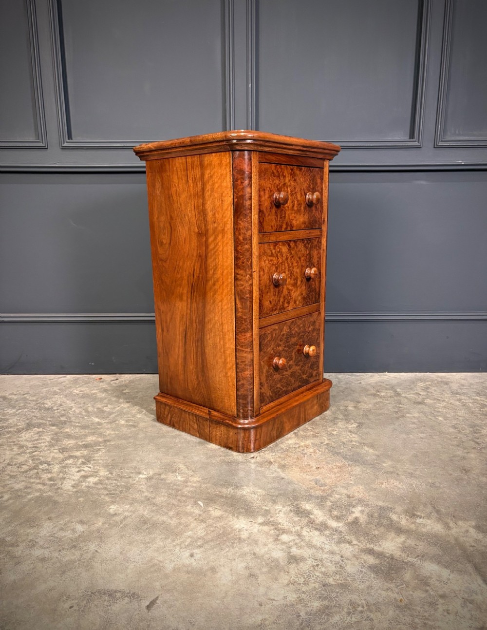 A matching pair of Victorian burr walnut bedside chests featuring three drawers each with turned wooden knobs and rounded plinth bases. View VI