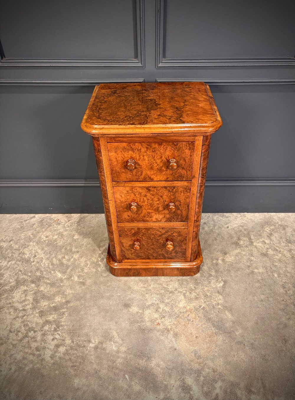 A matching pair of Victorian burr walnut bedside chests featuring three drawers each with turned wooden knobs and rounded plinth bases. View VII