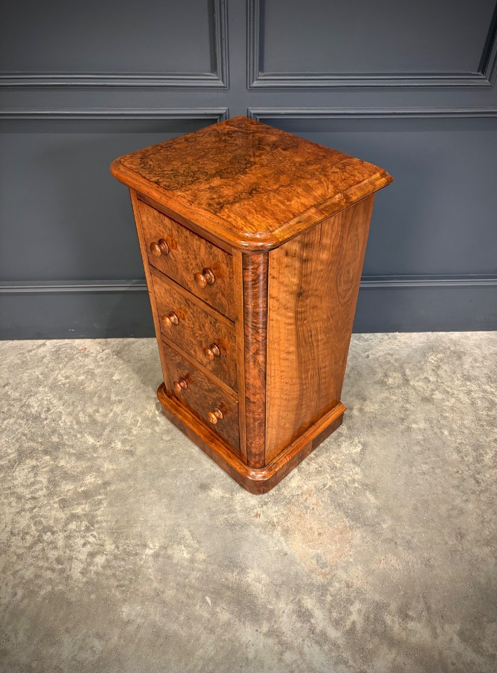 A matching pair of Victorian burr walnut bedside chests featuring three drawers each with turned wooden knobs and rounded plinth bases. View IX
