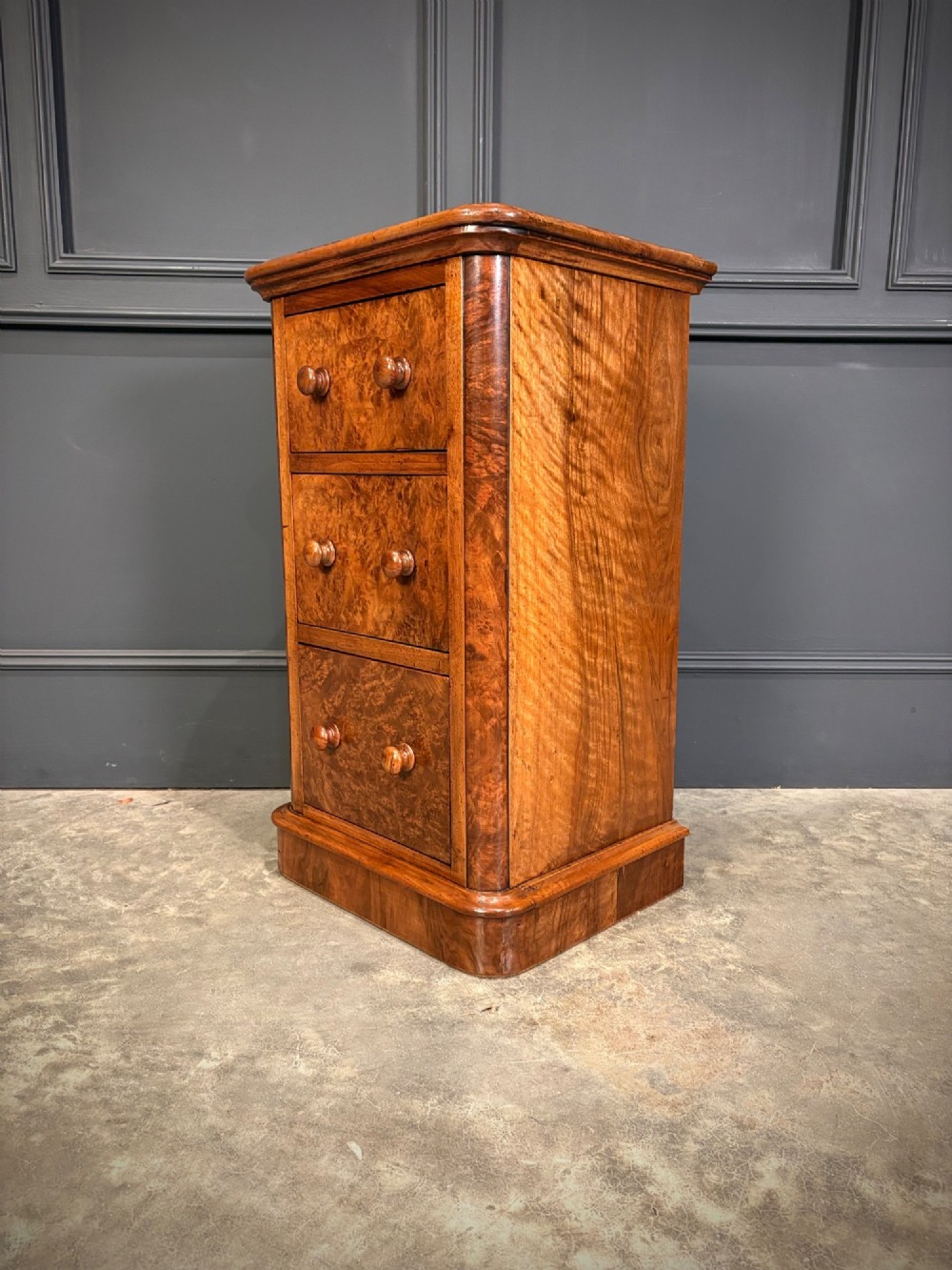 A matching pair of Victorian burr walnut bedside chests featuring three drawers each with turned wooden knobs and rounded plinth bases. View X