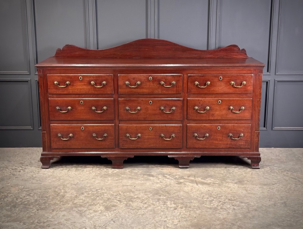 An 18th-century mahogany bank of nine drawers featuring a shaped upstand gallery back, brass swan-neck handles, and bracket feet.