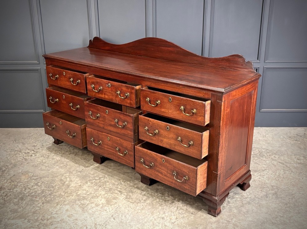 An 18th-century mahogany bank of nine drawers featuring a shaped upstand gallery back, brass swan-neck handles, and bracket feet. View IV