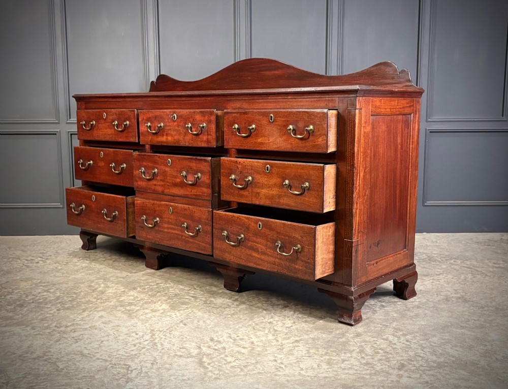 An 18th-century mahogany bank of nine drawers featuring a shaped upstand gallery back, brass swan-neck handles, and bracket feet. View V