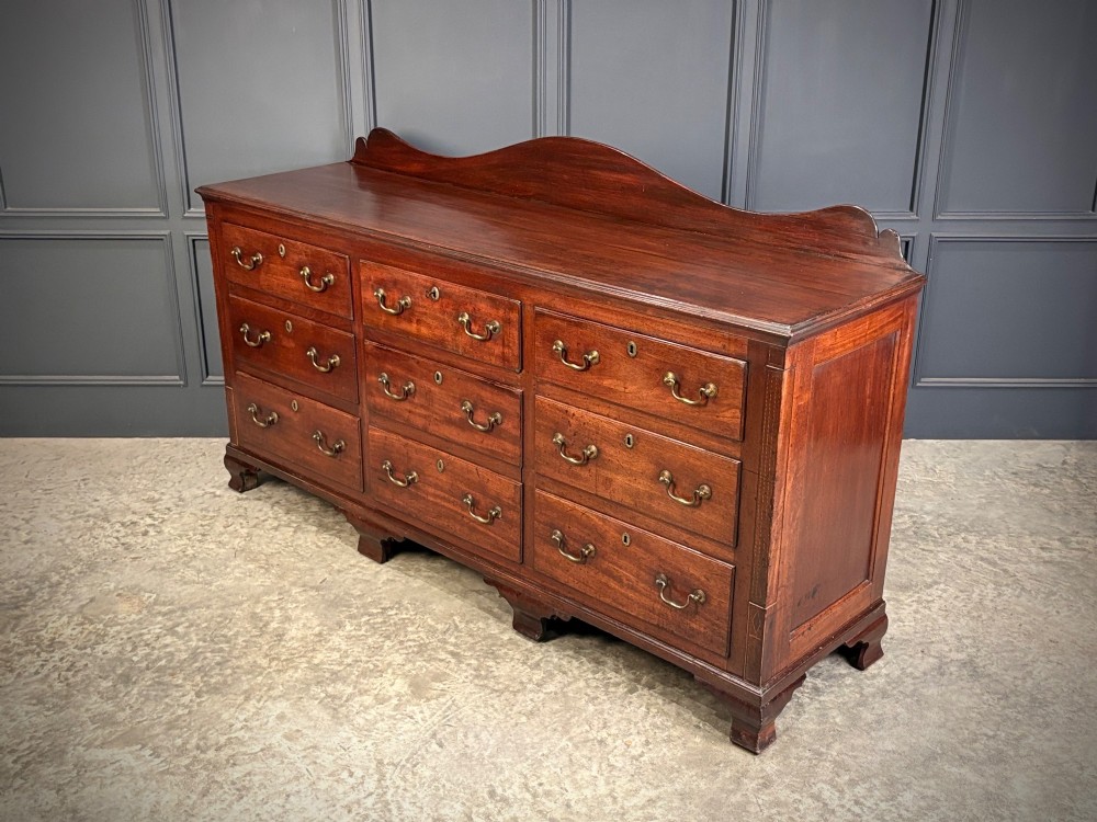 An 18th-century mahogany bank of nine drawers featuring a shaped upstand gallery back, brass swan-neck handles, and bracket feet. View VI