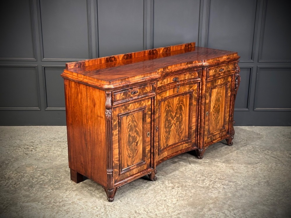 A flame mahogany Biedermeier sideboard featuring three upper drawers over three cupboard doors with symmetrical bookmatched wood grain patterns. View II
