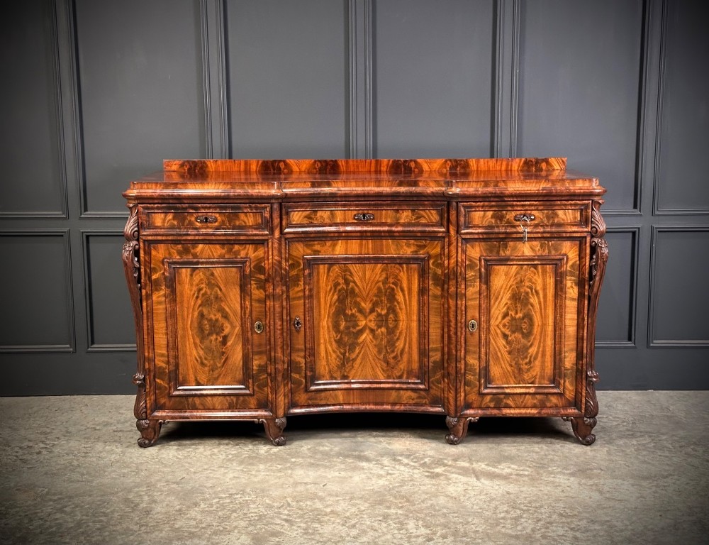 A flame mahogany Biedermeier sideboard featuring three upper drawers over three cupboard doors with symmetrical bookmatched wood grain patterns. View IV