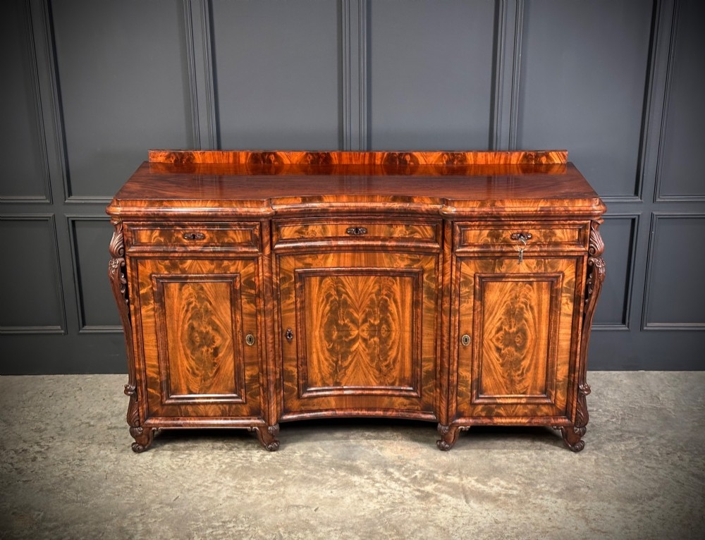 A flame mahogany Biedermeier sideboard featuring three upper drawers over three cupboard doors with symmetrical bookmatched wood grain patterns.