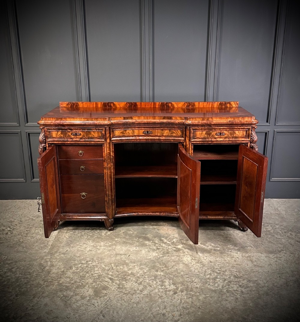 A flame mahogany Biedermeier sideboard featuring three upper drawers over three cupboard doors with symmetrical bookmatched wood grain patterns. View V