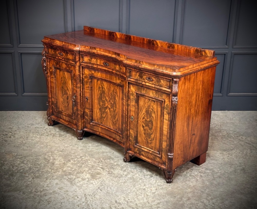A flame mahogany Biedermeier sideboard featuring three upper drawers over three cupboard doors with symmetrical bookmatched wood grain patterns. View VI