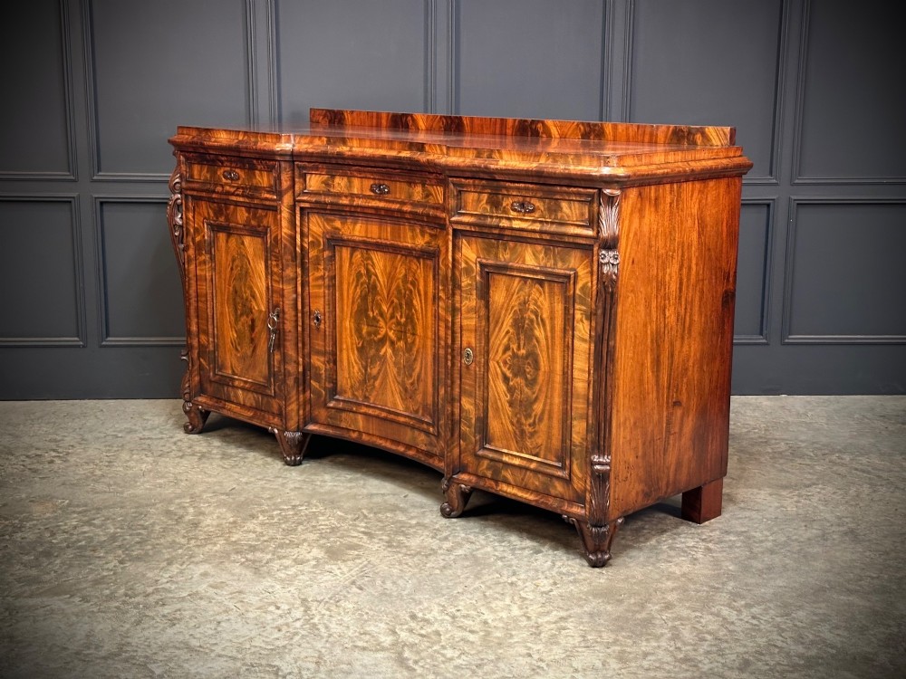 A flame mahogany Biedermeier sideboard featuring three upper drawers over three cupboard doors with symmetrical bookmatched wood grain patterns. View VII