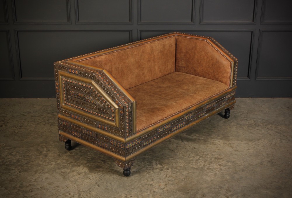 A boxy Moroccan-style sofa featuring tan leather upholstery on the seat and interior, surrounded by an exterior clad in embossed brass metal panels with decorative studding.