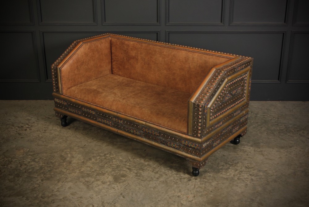 A boxy Moroccan-style sofa featuring tan leather upholstery on the seat and interior, surrounded by an exterior clad in embossed brass metal panels with decorative studding. View V