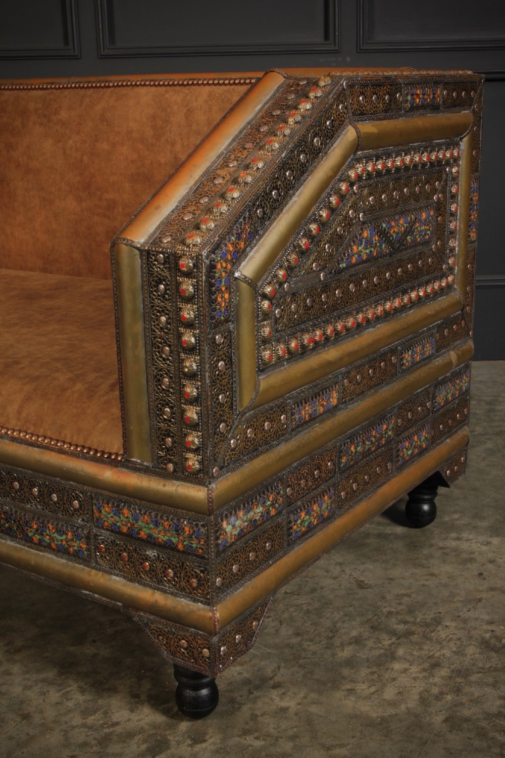 A boxy Moroccan-style sofa featuring tan leather upholstery on the seat and interior, surrounded by an exterior clad in embossed brass metal panels with decorative studding. View VII