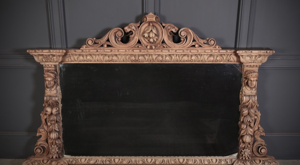 A wide Victorian oak overmantel mirror featuring detailed hand-carved cresting with beast heads, side pilasters with fruit swags, and carved human masks.