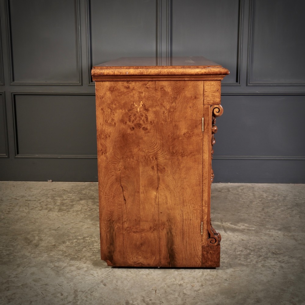 A 19th-century Victorian pollard oak sideboard featuring three relief-panelled cupboard doors, carved corbels, and a figure-rich timber surface. View XV