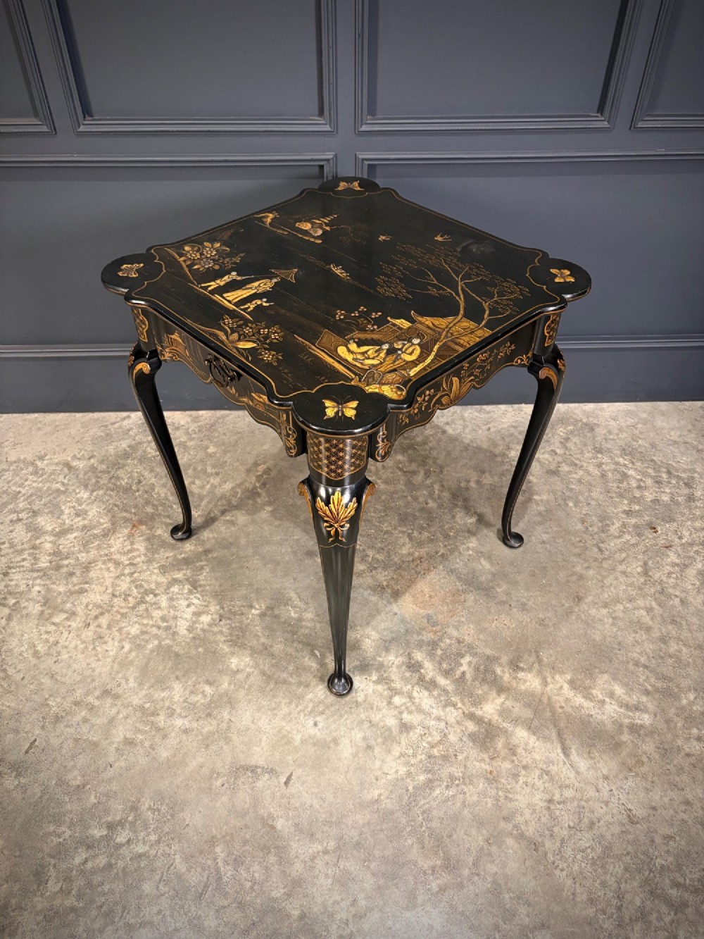 A black lacquered square occasional table featuring gilded Chinoiserie landscape scenes, shaped apron edges, a single drawer, and slender cabriole legs. View IV
