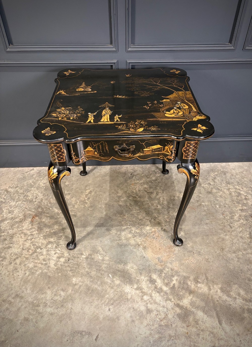 A black lacquered square occasional table featuring gilded Chinoiserie landscape scenes, shaped apron edges, a single drawer, and slender cabriole legs. View V