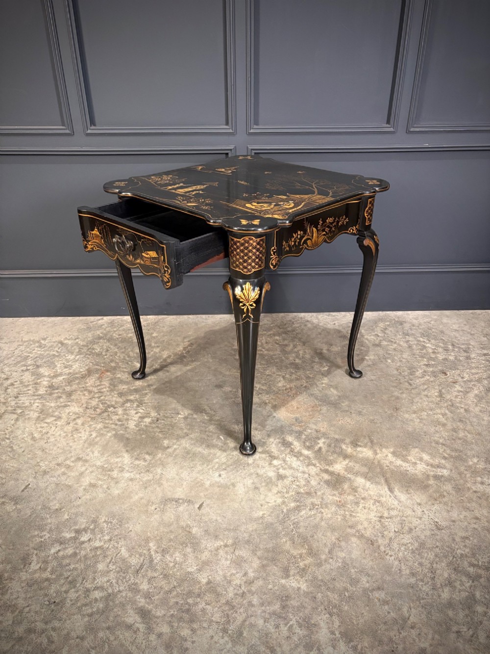 A black lacquered square occasional table featuring gilded Chinoiserie landscape scenes, shaped apron edges, a single drawer, and slender cabriole legs. View VIII