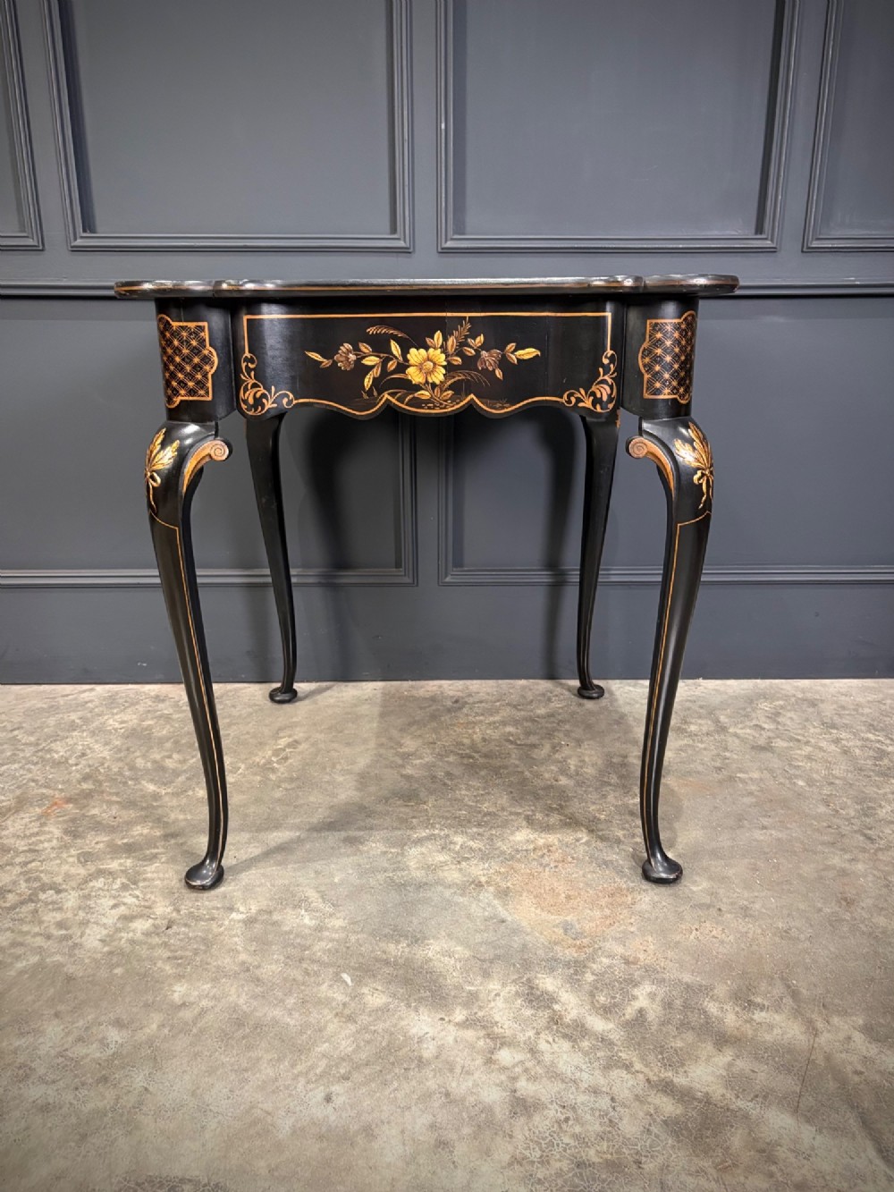 A black lacquered square occasional table featuring gilded Chinoiserie landscape scenes, shaped apron edges, a single drawer, and slender cabriole legs. View X