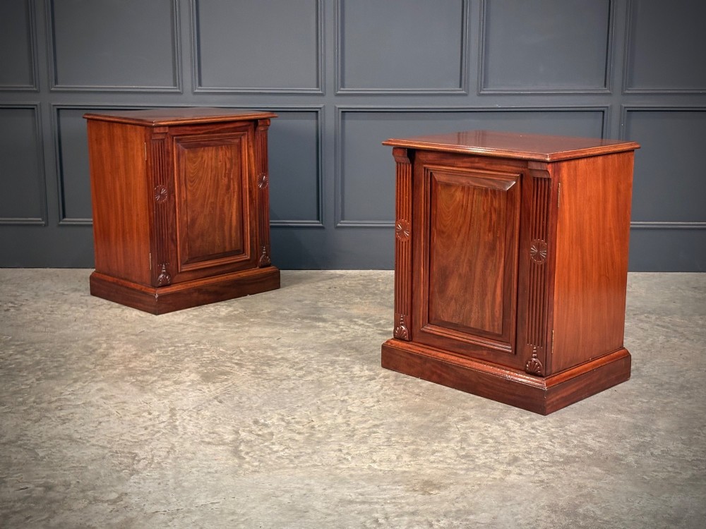 A matching pair of Victorian mahogany bedside cabinets featuring panelled doors with flame veneer and carved fluted pilasters on plinth bases. View II