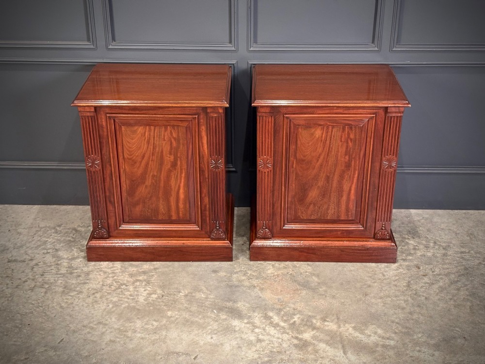 A matching pair of Victorian mahogany bedside cabinets featuring panelled doors with flame veneer and carved fluted pilasters on plinth bases. View IV