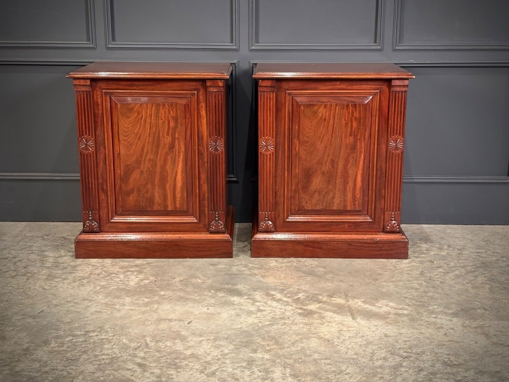 A matching pair of Victorian mahogany bedside cabinets featuring panelled doors with flame veneer and carved fluted pilasters on plinth bases.