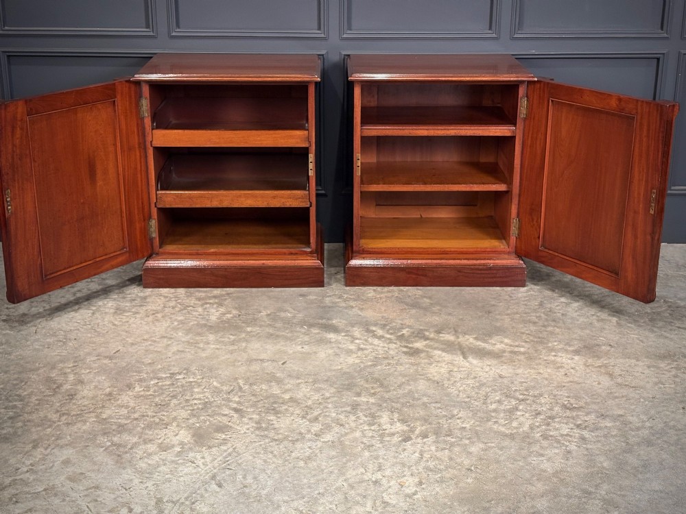 A matching pair of Victorian mahogany bedside cabinets featuring panelled doors with flame veneer and carved fluted pilasters on plinth bases. View V