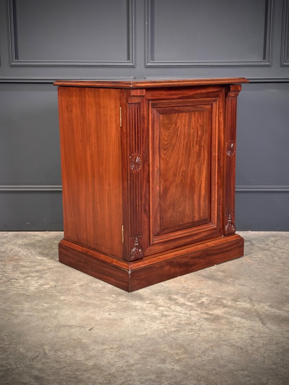 A matching pair of Victorian mahogany bedside cabinets featuring panelled doors with flame veneer and carved fluted pilasters on plinth bases. View VI