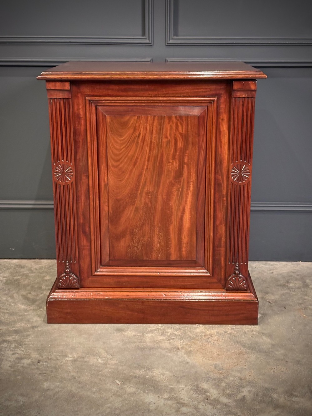 A matching pair of Victorian mahogany bedside cabinets featuring panelled doors with flame veneer and carved fluted pilasters on plinth bases. View VII