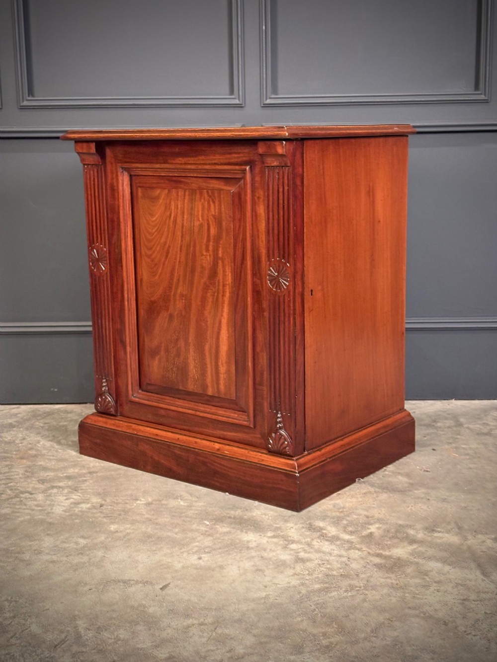 A matching pair of Victorian mahogany bedside cabinets featuring panelled doors with flame veneer and carved fluted pilasters on plinth bases. View VIII