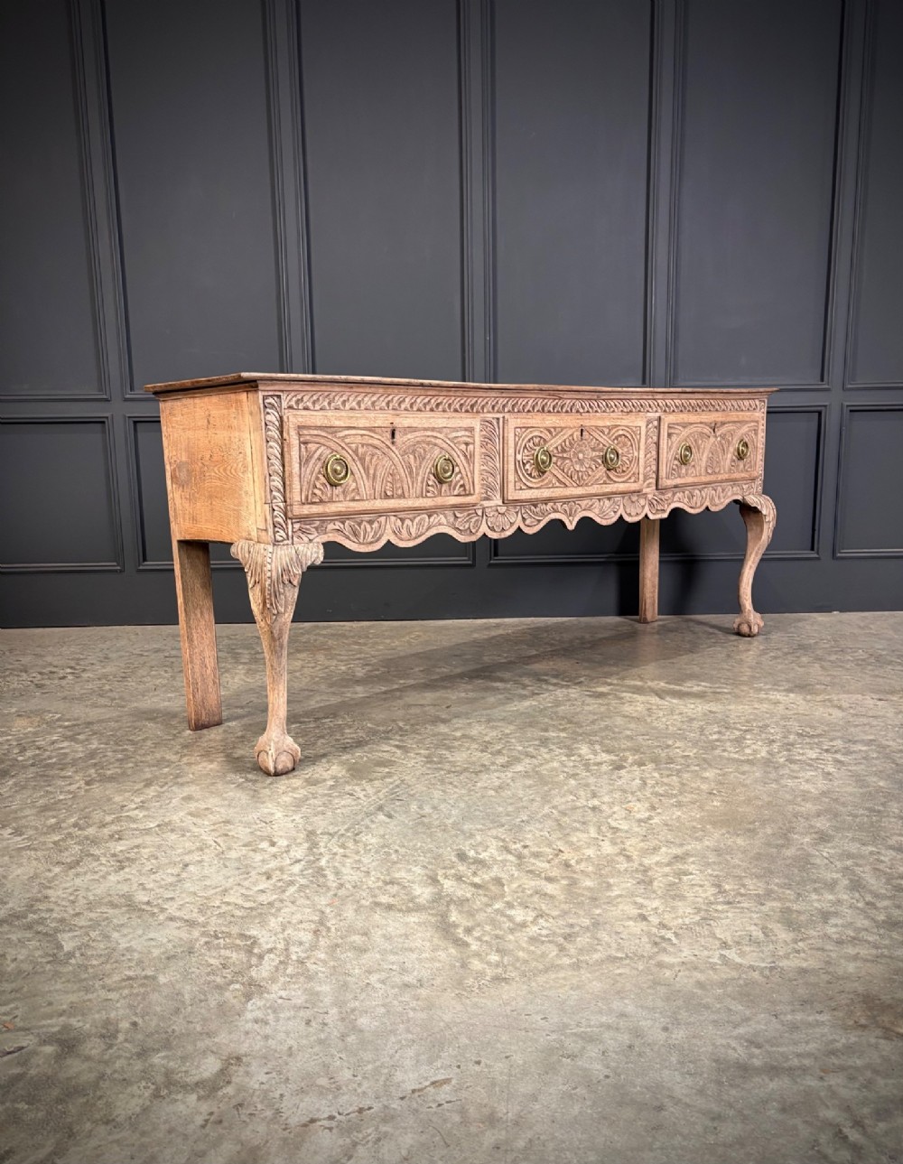 An 18th-century carved oak dresser base with three carved drawer fronts, a decorative apron, cabriole front legs, and claw and ball feet.