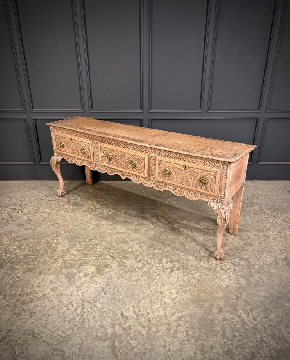 An 18th-century carved oak dresser base with three carved drawer fronts, a decorative apron, cabriole front legs, and claw and ball feet. View VII